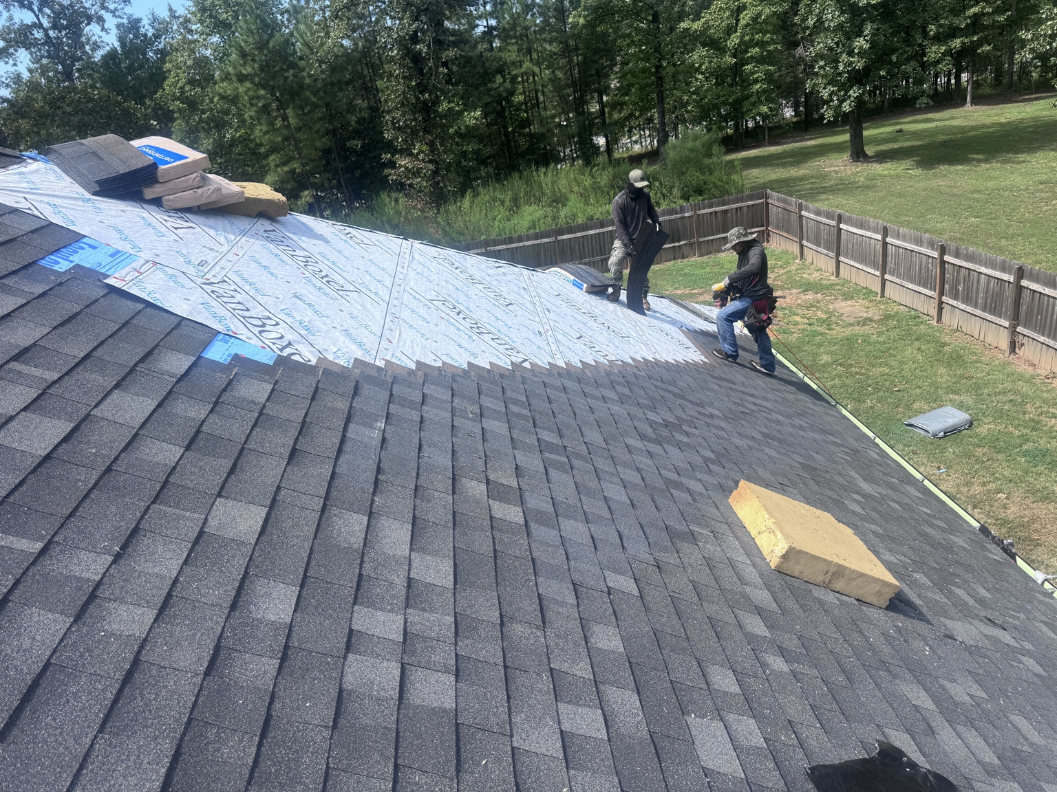 Roofers installing dark shingles over underlayment on a sloped roof