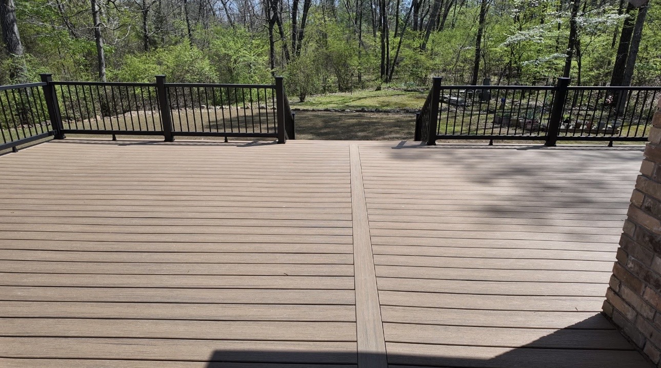 Composite deck boards and black railing overlooking a wooded backyard